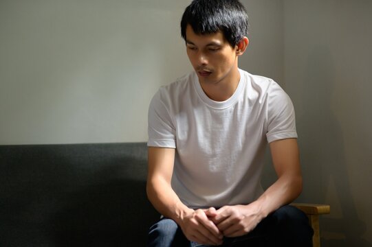 Reflective Young Man Sitting on Couch in Minimalist Interior Space