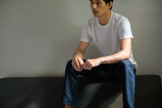 Thoughtful Young Man in Plain T-Shirt Sitting on Sofa