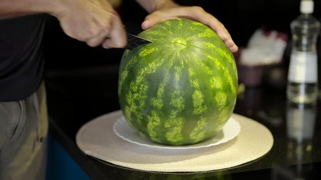 Person Cutting Whole Green Watermelon With Kitchen Knife On Table. Fresh Fruit Slicing. Healthy Eating 