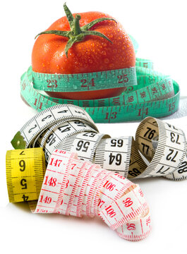 Tomato surrounded by measuring tapes with numbers showing various measurements on a white background