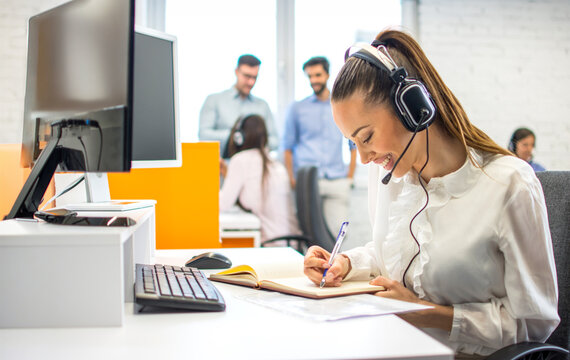 Focused young businesswoman writing notes in notebook at office desk