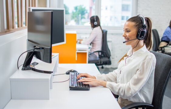 Cheerful female support operator working at computer in call center