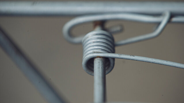 Close up of metal coil spring mechanism on steel wire frame.A detailed macro shot focusing on a sturdy grey metal coil spring mechanism wrapped around a steel bar. 