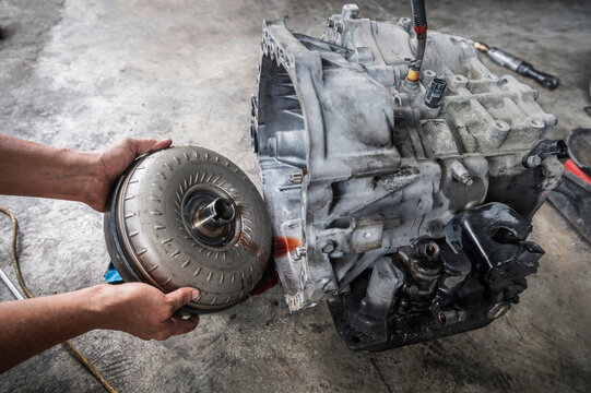 Auto mechanic removing a torque converter from an automatic transmission.