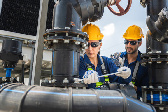 Engineers maintaining industrial piping system at facility outdoors, Workers checking water cooling system valves and pipes, Industrial technicians with wrench inspecting water pipeline and equipment