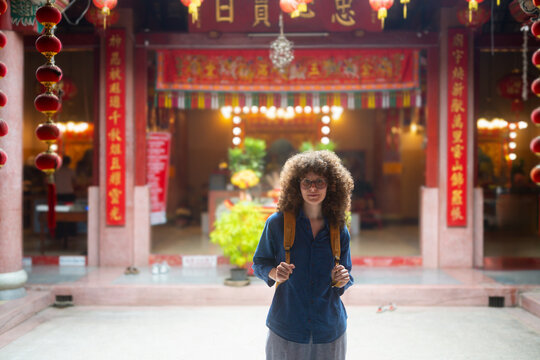 Young Caucasian Woman Traveler with Curly Hair and Backpack Standing at Chinese Temple Entrance