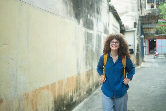 Happy Caucasian Woman Traveler with Backpack Walking Through Narrow Asian Street Alley
