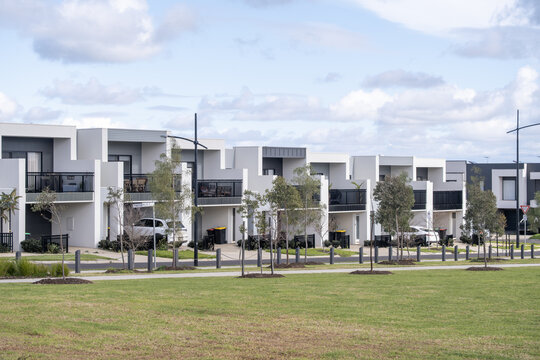 A uniform row of modern, contemporary two-story townhouses facing a grassy public reserve in an outer suburb of Melbourne, Australia. Suburban housing design, medium-density residential development