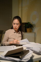 Fototapeta premium Stressed Businesswoman Working Late Night Reviewing Documents with Tension at Messy Office Desk