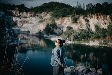 Fototapeta premium Female traveler standing on rock with head tilted back enjoying fresh breeze at quarry lake.