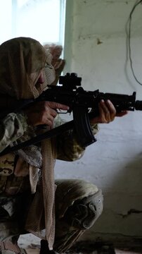 A soldier in camouflage clothing takes his weapon off safety, cocks the bolt, then raises his automatic rifle and aims at the enemy. Slow motion vertical 4k footage.