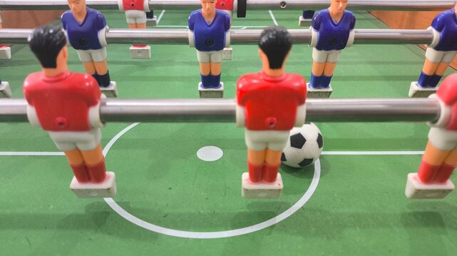Close up of colorful miniature football players competing around a soccer ball on a foosball table, showcasing strategy, teamwork, competition, recreation, sports entertainment