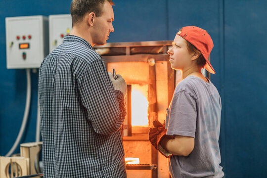 Man teaches student glassblowing by hot furnace