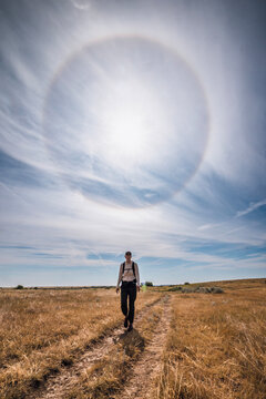 Woman hikes on a dirt trail under a large sun halo