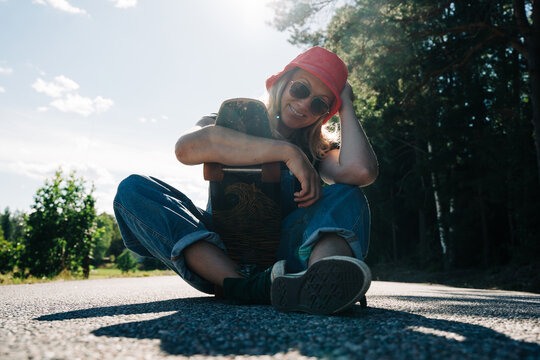 Smiling woman with longboard skateboard sitting on a sunny road
