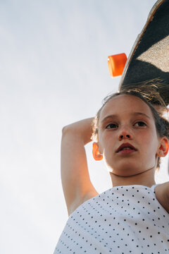 Low angle view of a girl with freckles holding her skateboard