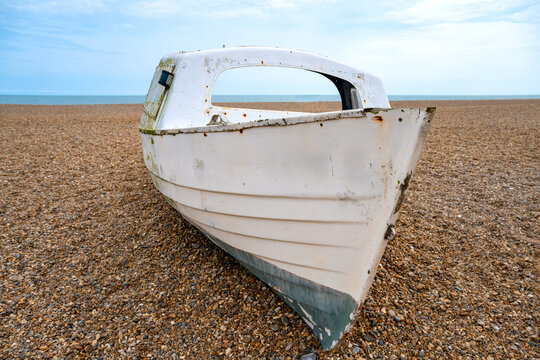 A weathered old fishing boat rests on the shingle beach at Aldeburgh, Suffolk, its white hull worn and rusted. The tranquil North Sea stretches to the horizon behind it on England's East Anglian coast