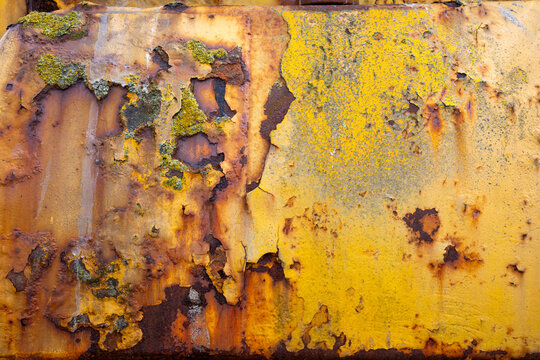 Close-up of rusted, peeling yellow paint on an old tractor used to launch boats on Aldeburgh beach, Suffolk, its weathered metal surface covered in patches of lichen and corrosion.