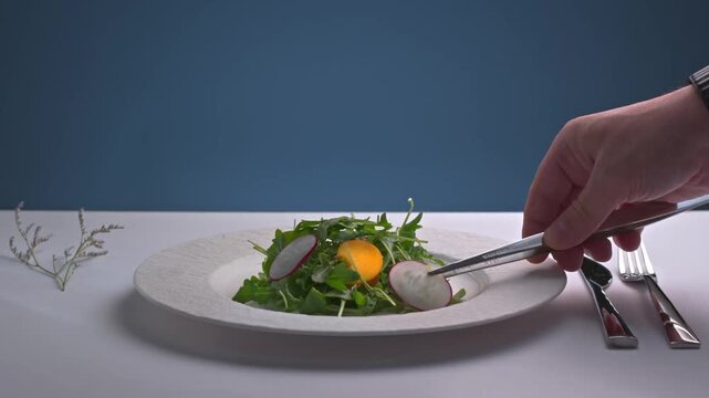 Chef styling fresh green vegetable salad plate with tweezers in restaurant kitchen