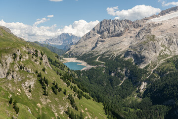 Obraz premium Arabba, Italy. Panoramic alpine landscape overlooking Lago di Fedaia reservoir, forested Dolomite valleys and the Marmolada mountain massif