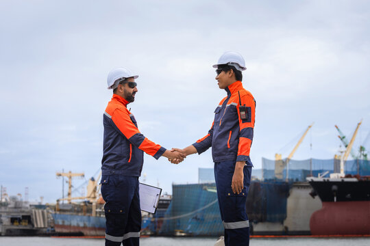 Maritime supervisors in safety gear greeting each other outdoors, Logistics workers handshake with cargo ship background at dock, Port engineers shaking hands after successful business deal at harbor