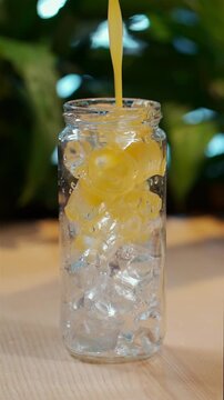 reverse video of pouring yellow juice in glass bottle with ice or prepare drink