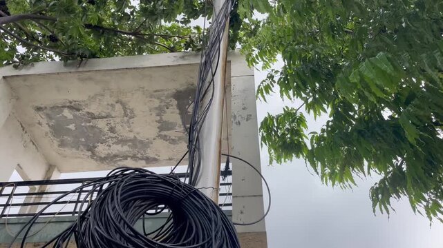 Large Coil of Black Electrical Cables Mounted on Outdoor Building iron pole