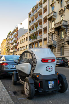 Milan, Italy - January 16 2019: Compact electric microcar parked on a street surrounded by conventional cars and historic residential architecture. Electric mobility in a dense European city.