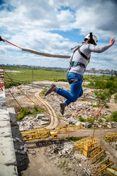 Woman in helmet rope jumping with arms spread over demolition site, city skyline visible in background, extreme sport adrenaline and thrill concept