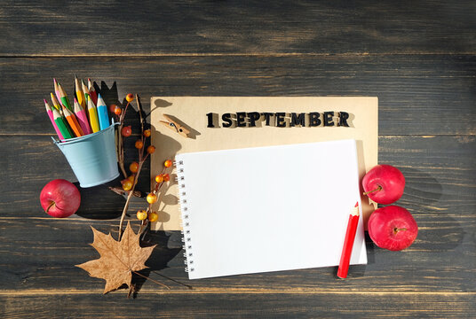 September calendar. date 1 September made of wooden letters, pencils, empty notepad, fallen leaf and red apples close up on brown wooden table background. top view. copy space. back to school concept