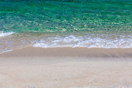 Emerald sea and sandy shore. Clear turquoise water lapping a pale sand beach. Horizontal composition. Calm, shallow coastal scene.