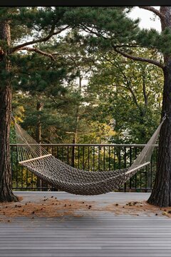 Hand-woven natural fiber hammock suspended between two pines on a wooden terrace in a serene forest retreat during autumn light