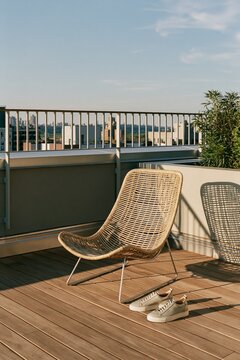 Leather sneakers placed beside a rattan lounge chair on an urban rooftop deck during warm afternoon light, showcasing a serene outdoor setting