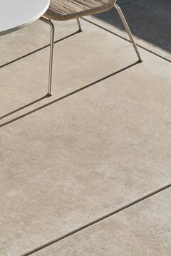 Closeup of textured concrete deck on an urban rooftop with a metal chair leg casting a shadow, illuminated by soft natural light