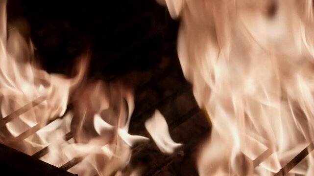 Meat searing on a grill grate as bright flames rise across a dark smoky background