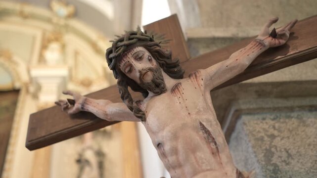 Close up of a polychrome Christ figure on a wooden cross inside a baroque church