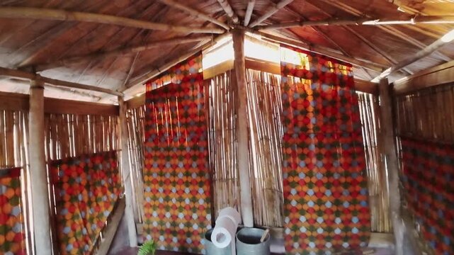 Spacious outdoor composting toilet features bamboo walls, colorful curtains, a covered roof and an open side overlooking a scenic tropical view.
