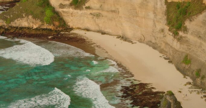 Turquoise ocean water crashing on a white sand beach near steep cliffs in Nusa Penida Bali