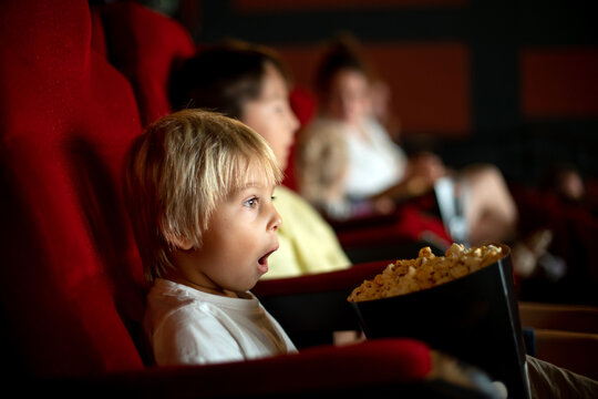 Cute child, boy, watching movie in a cinema, eating popcorn and enjoying