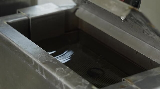 Jeweller hands placing a small band into a liquid tank basket at a workshop bench