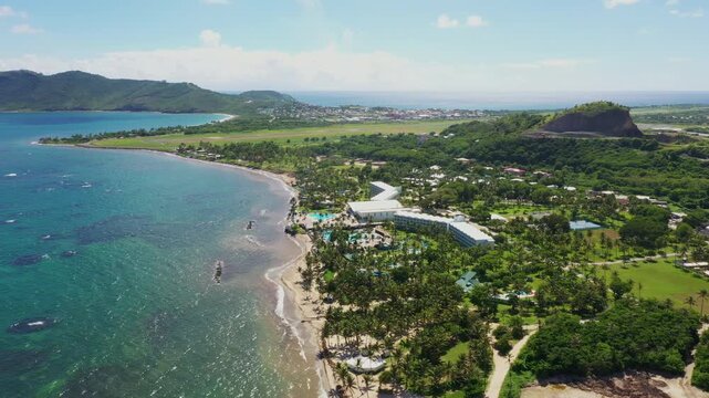 Cinematic drone shot from Vieux Fort Lighthouse, Saint Lucia, showcasing Coconut Bay Resort along the coastline, framed by verdant hills and the Caribbean Sea.