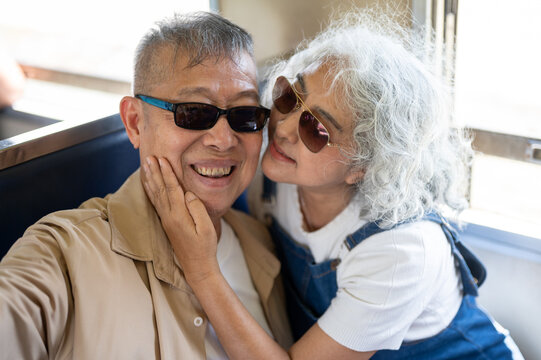 Asian senior elderly woman affectionately touching her partner face during a vintage train trip.