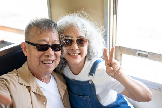 Asian senior couple taking a selfie and making a peace sign on a train