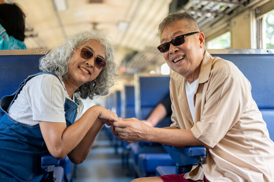 Asian senior elderly couple playfully holding hands while enjoying a romantic train adventure.