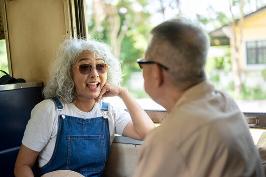 Asian senior elderly couple enjoying a friendly conversation during a relaxing train journey.