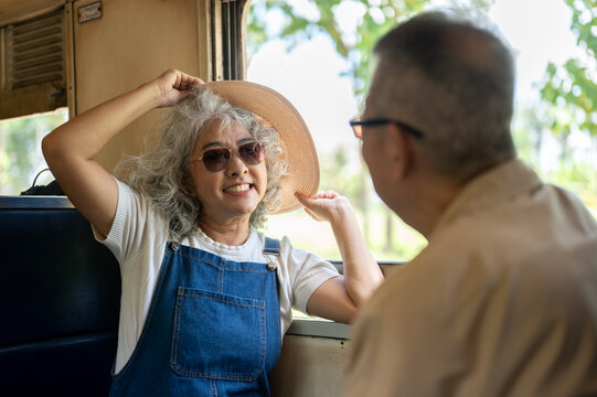 Senior woman wearing a sun hat enjoying a train journey with her husband