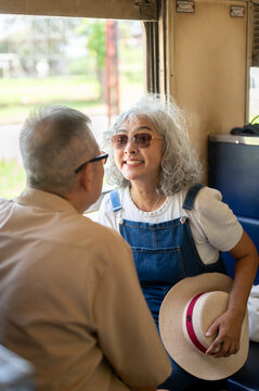Asian senior elderly woman smiling and chatting with her partner while holding a sun hat on a train.