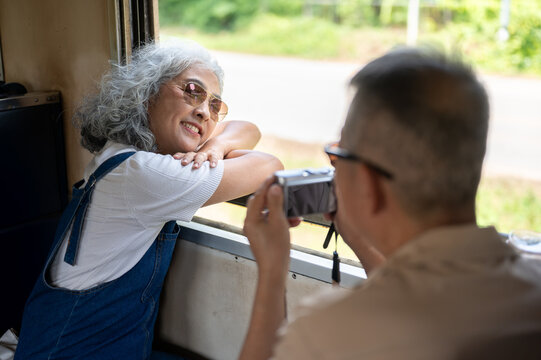Asian senior couple traveling by train, elderly woman enjoying journey while photographed by husband