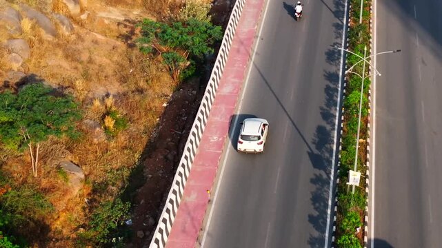 Close up shot of car moving on broken white line road with traffic flow, sign boards and footpath at khajaguda, hyderabad, telangana, india. day time, bird eye view, push in shot, drone shot, 4k.