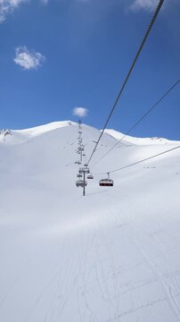 Personal perspective riding a gondola and chairlift system up snow covered mountain towards summit on a bright sunny day with. Winter vacation in the mountains